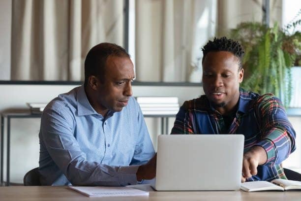 istockphoto-1329936192-612x612 Two African American employees working on project together, using laptop pointing at screen, discussing strategy and sharing ideas at meeting, colleagues involved in teamwork, cooperation concept